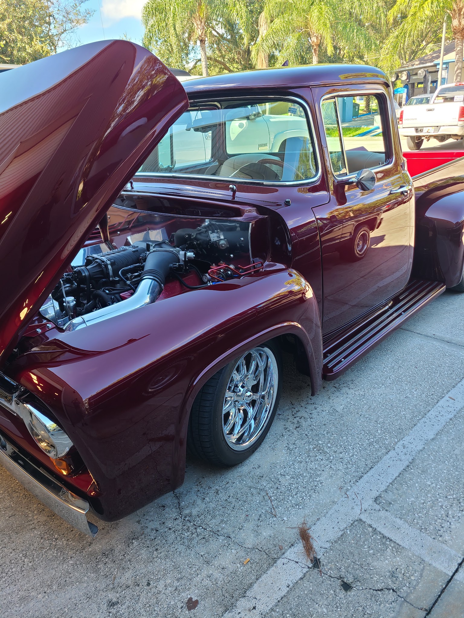 Maroon classic Ford F-100 pickup with hood up showing engine swap and chrome wheels