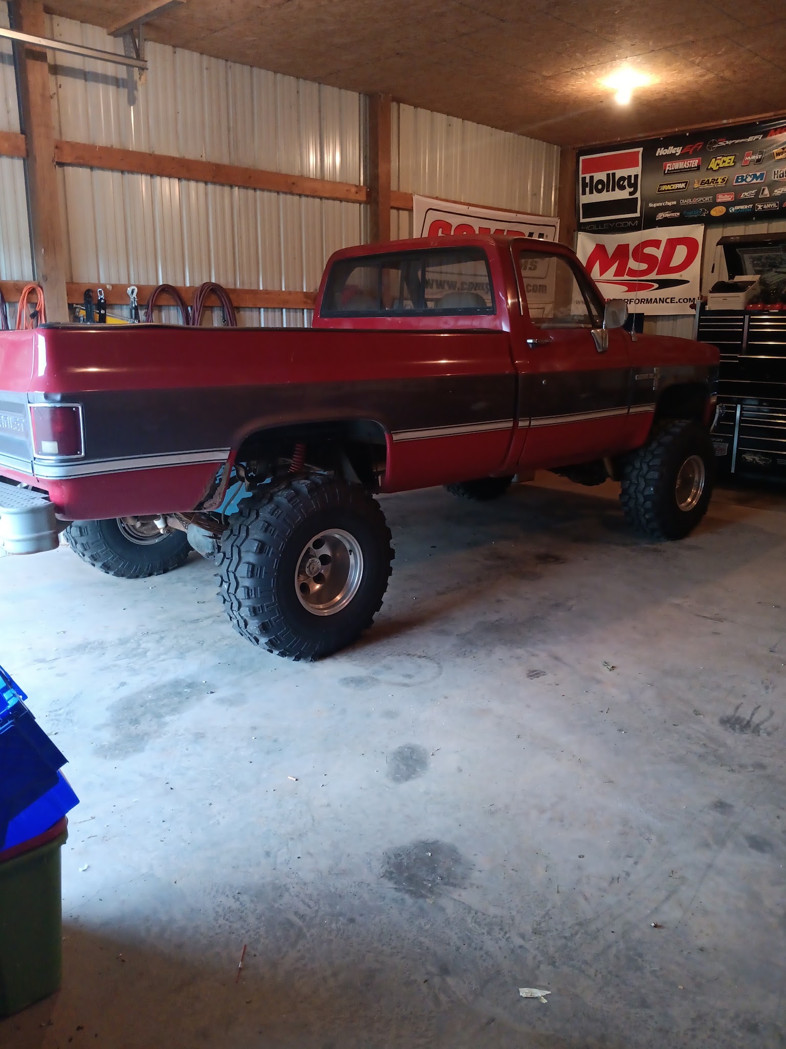 Lifted Chevy K10 pickup truck in the shop with Holley and MSD banners on the wall